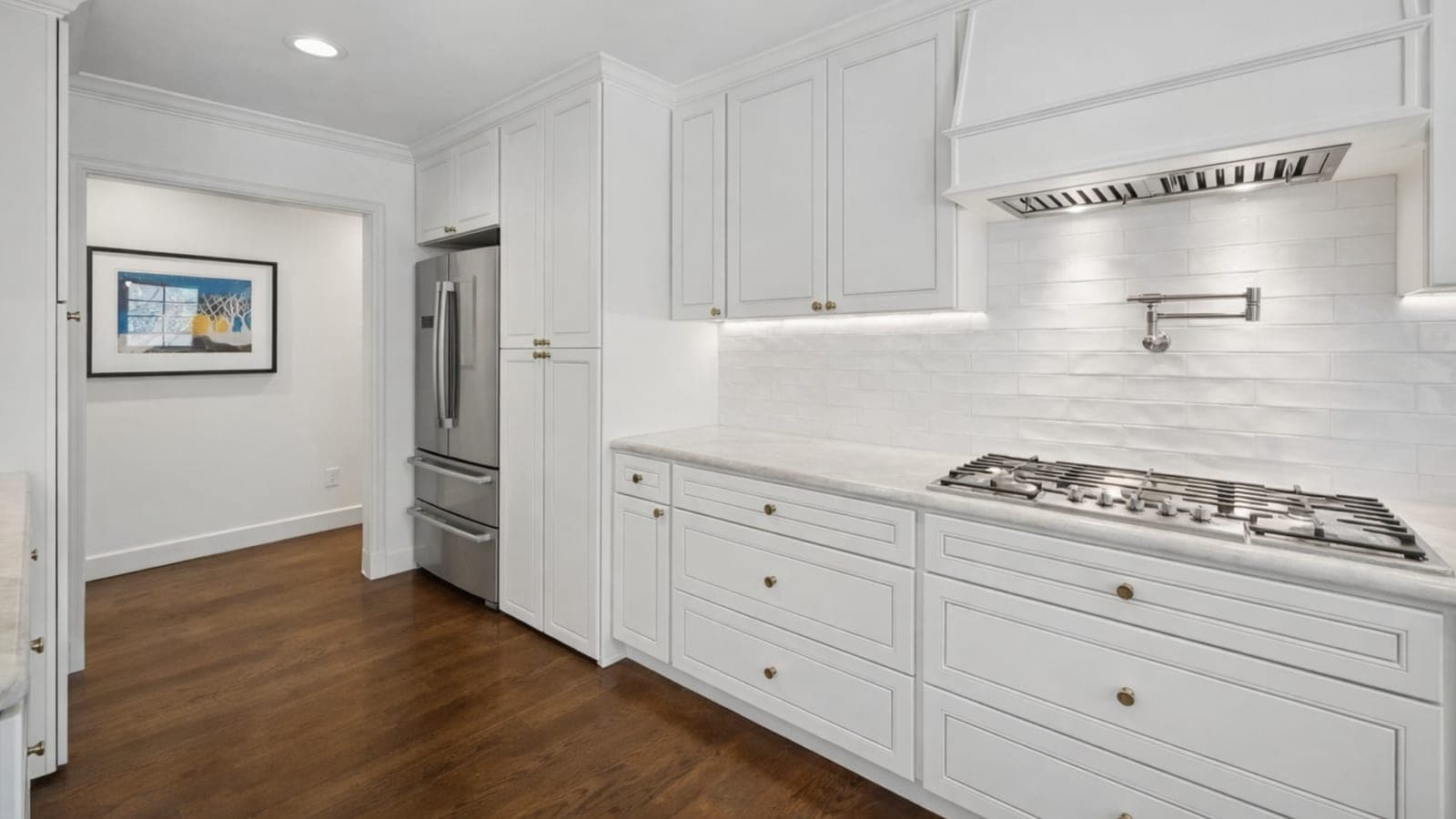 Remodeled white kitchen in Oak Cliff, Dallas, with a marble-topped island, two bar stools and hardwood floors
